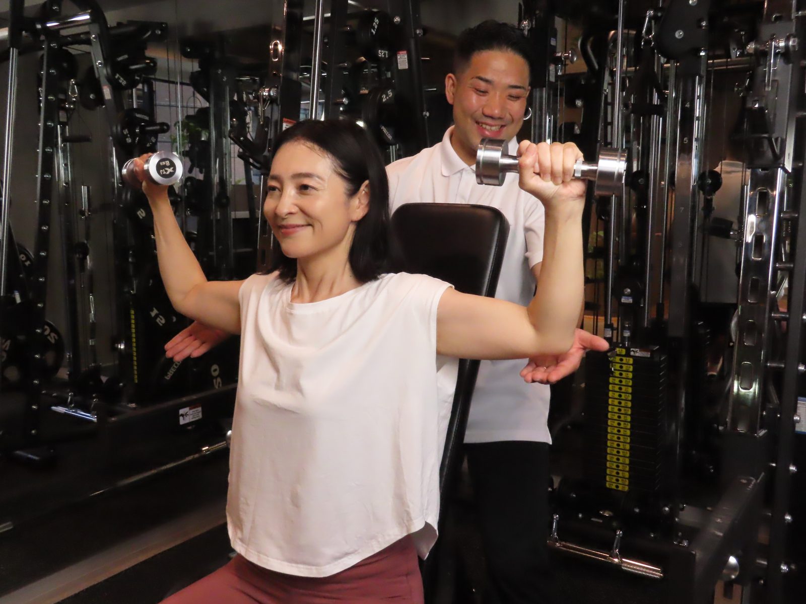 Physio+で、トレーナーが腕を支えながらダンベルでのトレーニングを指導する様子