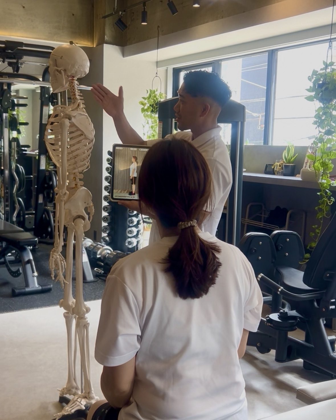 Physio+の理学療法士が骨格模型とタブレットの姿勢分析を使って身体の状態を説明する様子