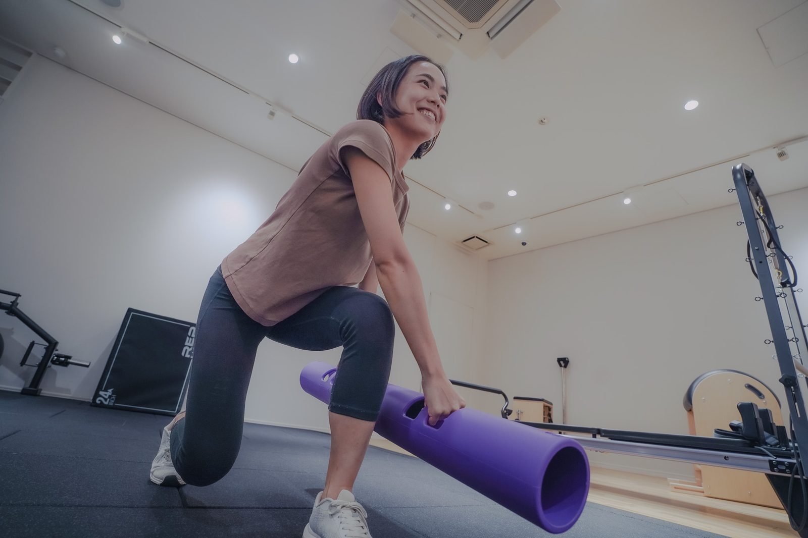 YOUTRALのスタジオで、女性が笑顔でトレーニングチューブを持ってランジをする様子